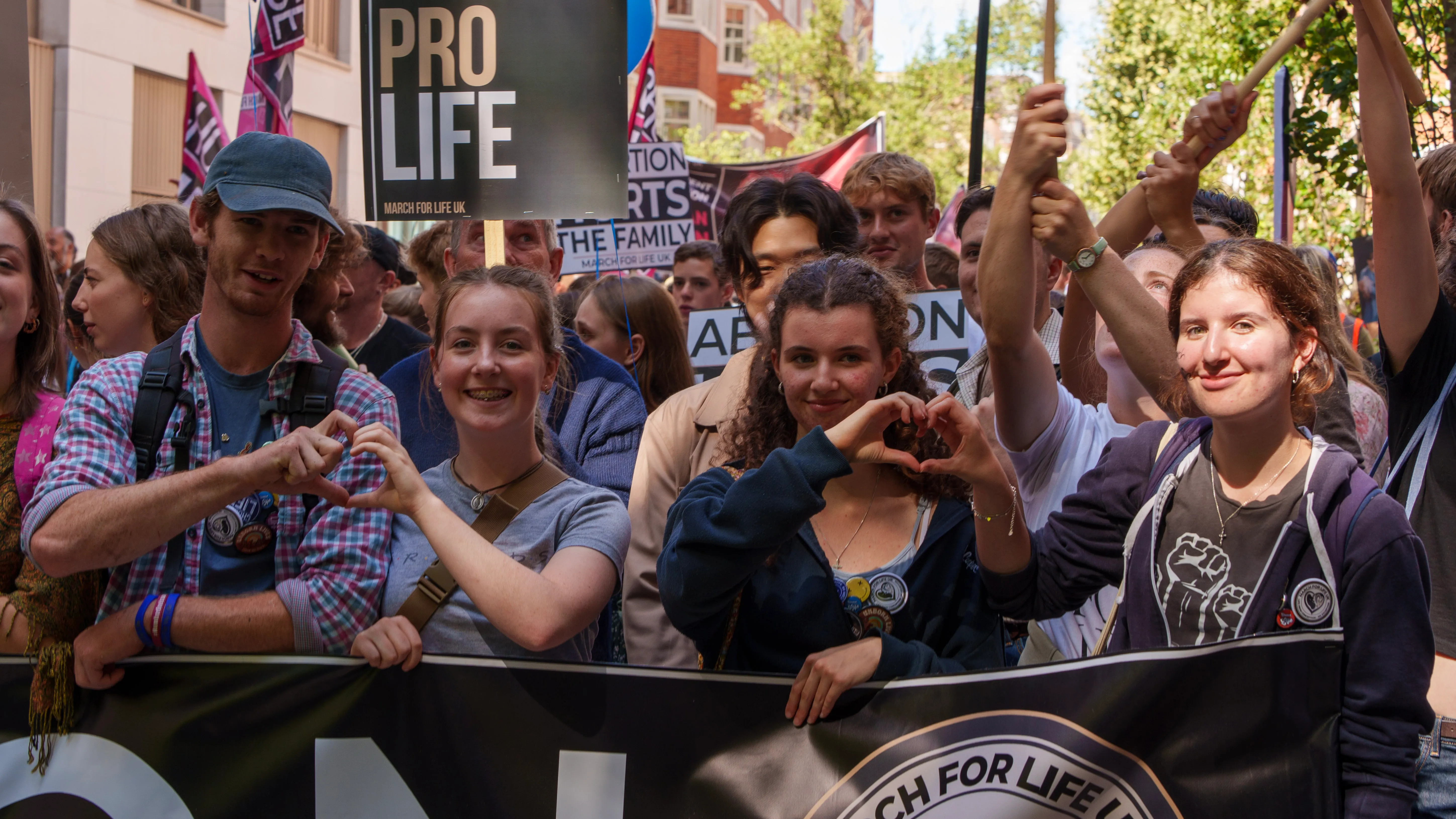 Young marchers forming heart shapes with their hands behind a March for Life UK banner