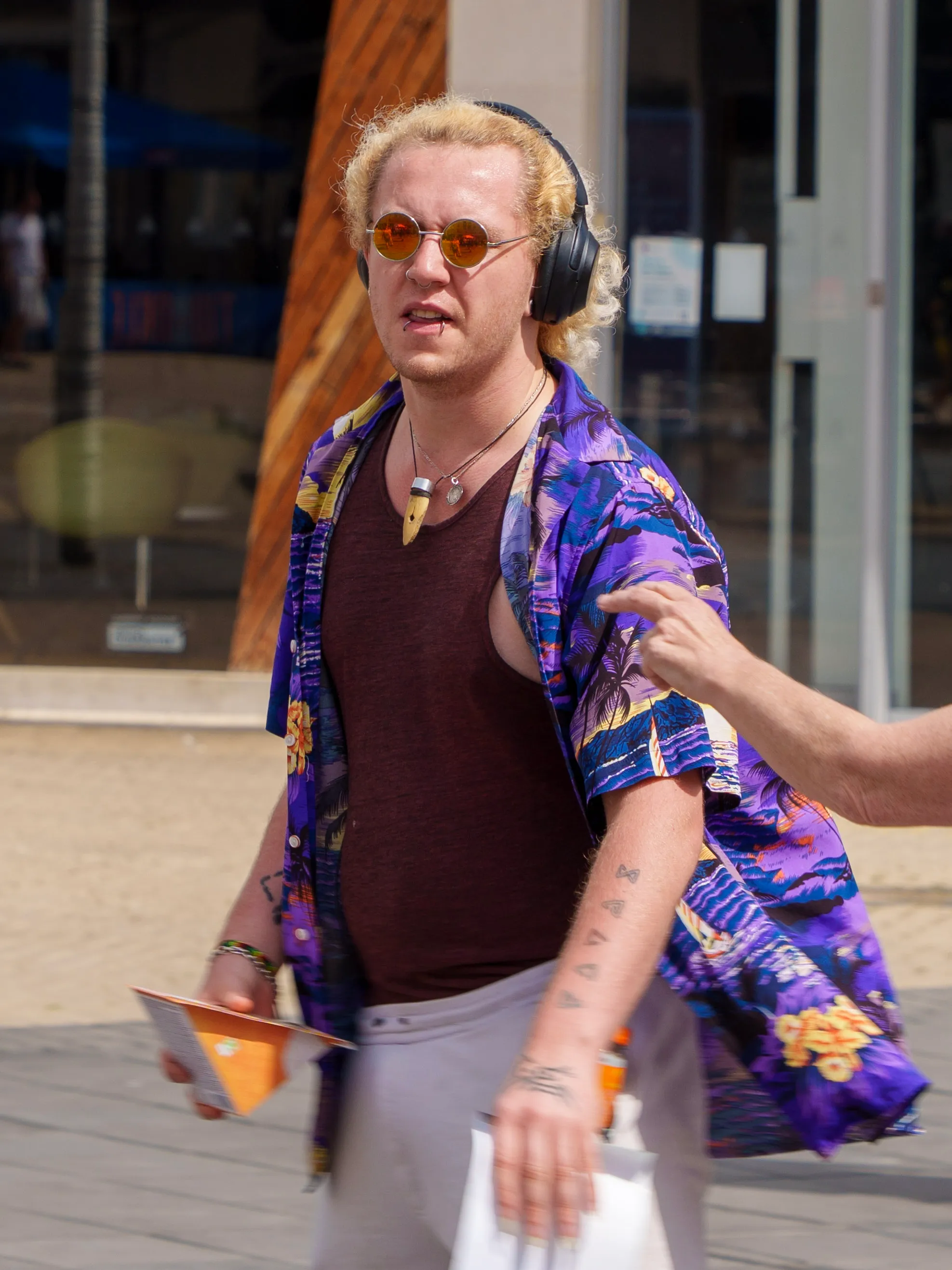 Street portrait of a young man with bleached curls, round sunglasses, and a tropical print shirt