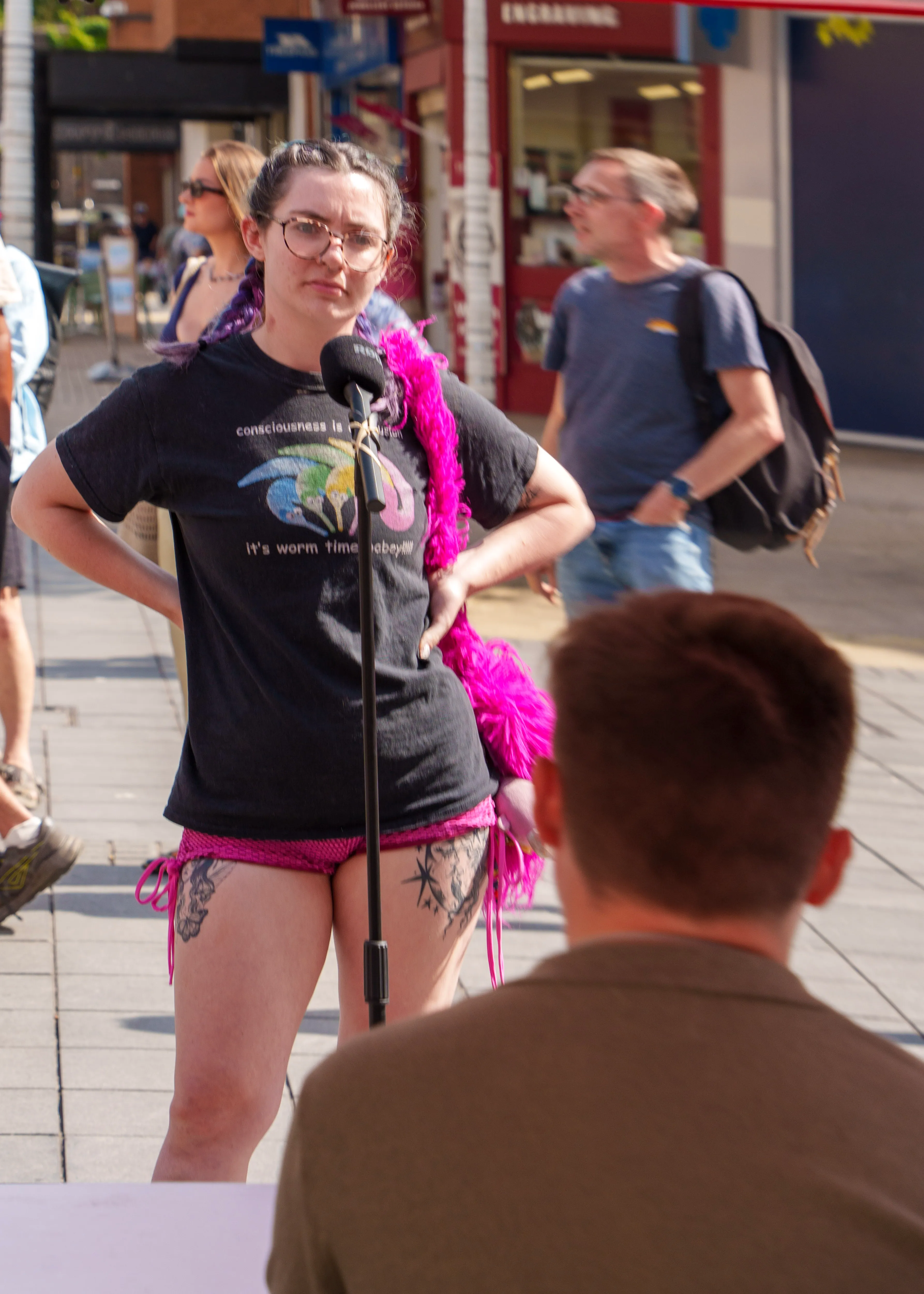 Candid portrait of a speaker in a pink feather boa at an outdoor microphone
