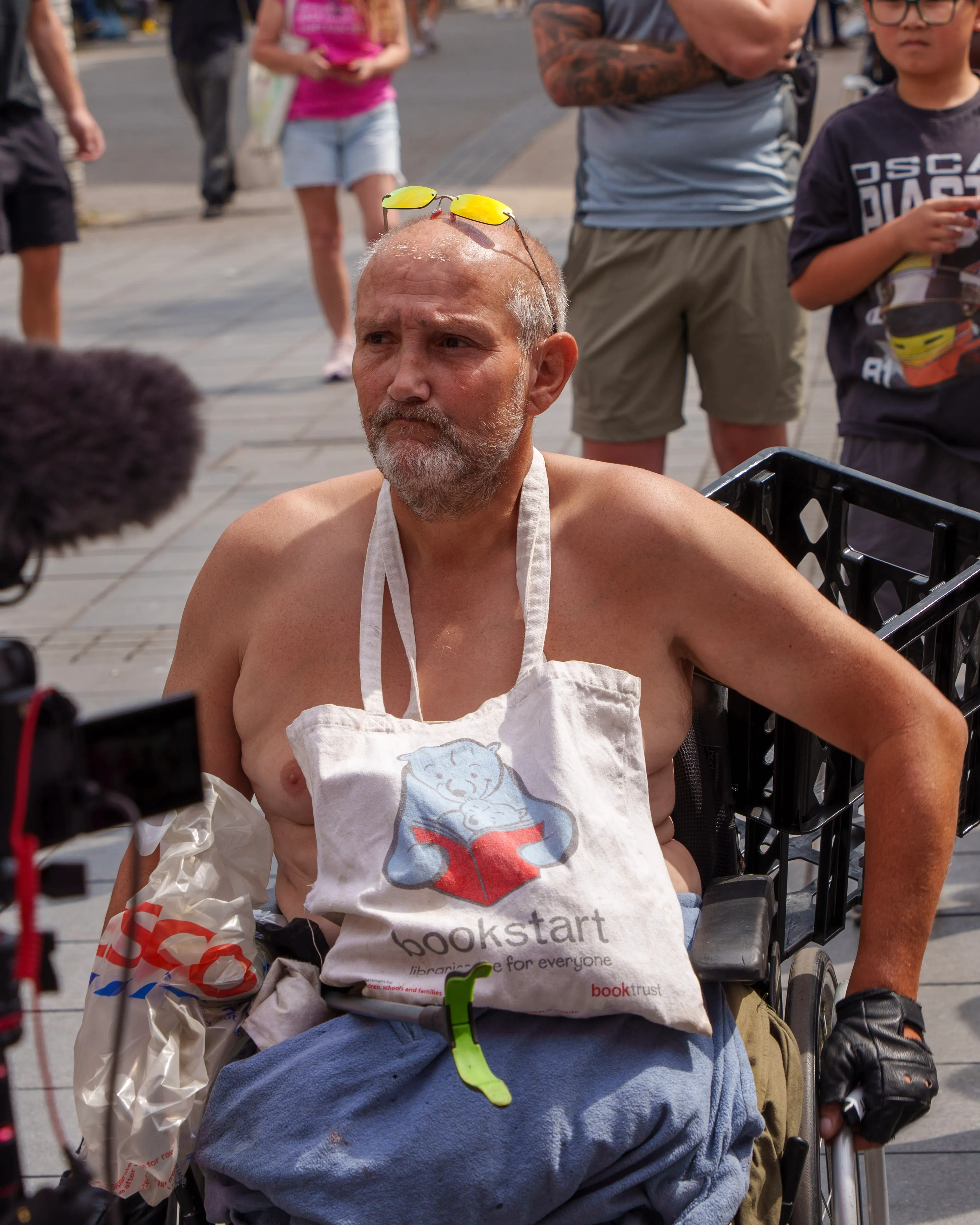 Documentary portrait of a man in a wheelchair outdoors, Bookstart tote draped across his chest